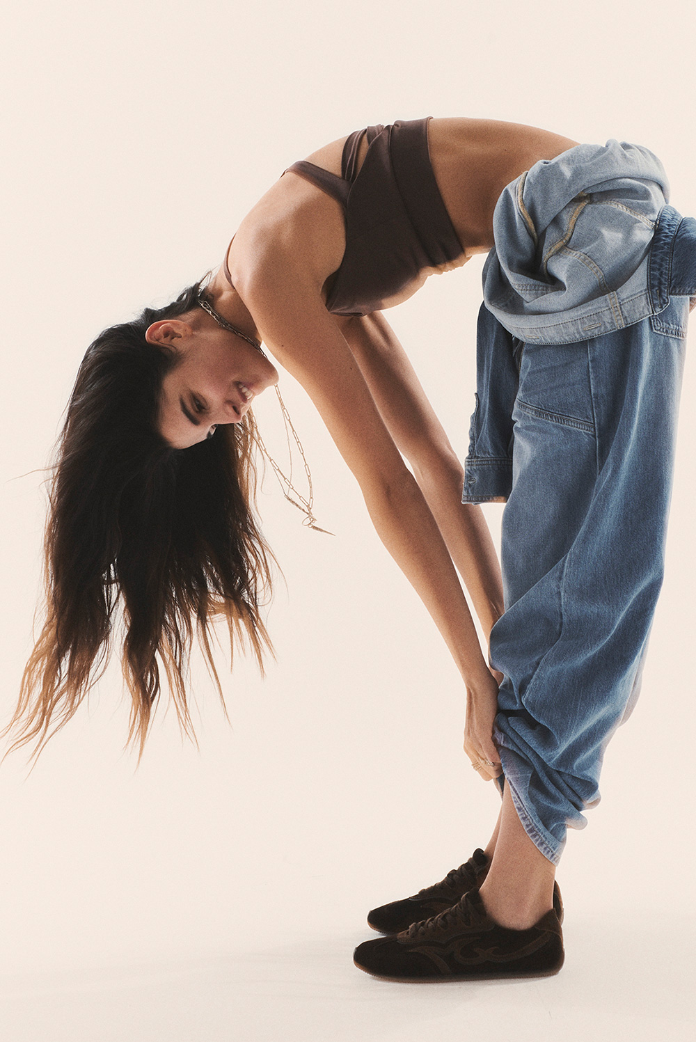 Brunette model wearing a blue jeans jumpsuits with brown bra